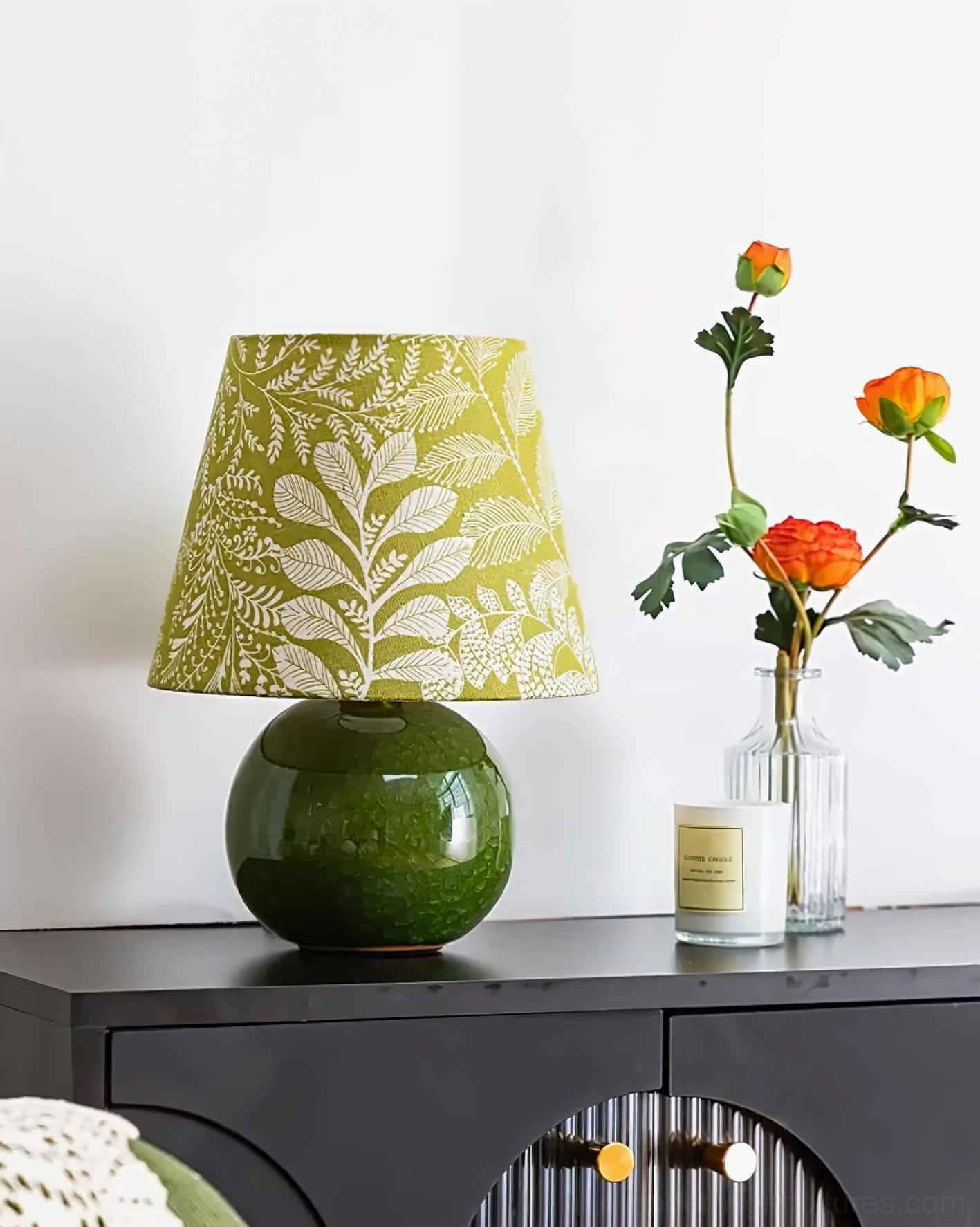 Green ceramic botanical table lamp styled with vase and decorative items on wood cabinet