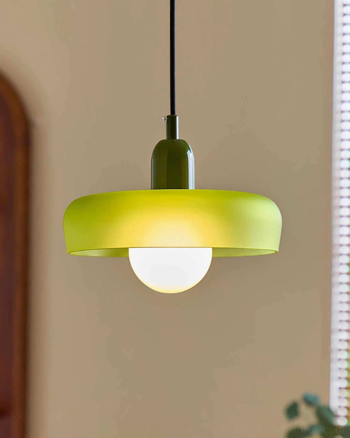 Green donut pendant light three-quarter front view with louvered window background, showing minimalist retro modern design and soft diffused lighting