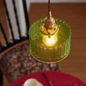 Close-up detail of green pendant light with brass socket and twisted fabric suspension cord illuminated