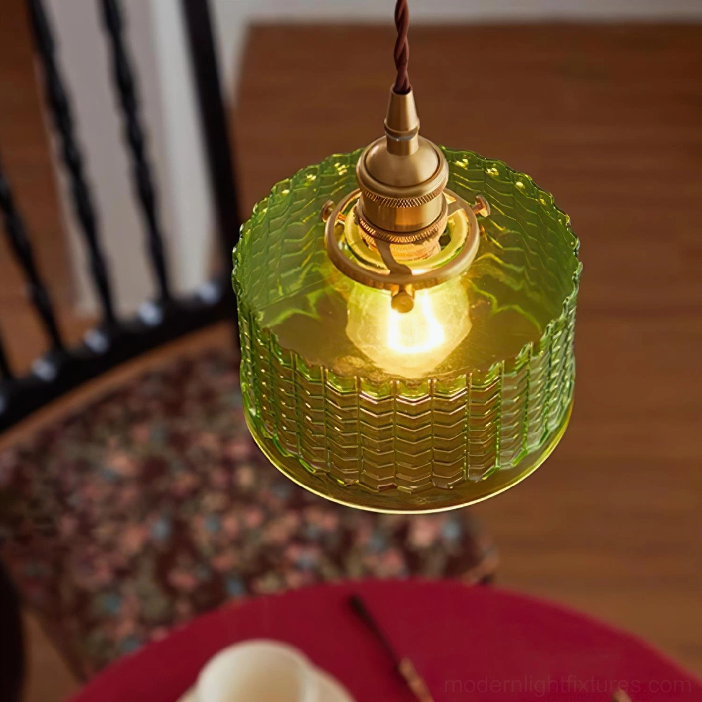 Close-up detail of green pendant light with brass socket and twisted fabric suspension cord illuminated