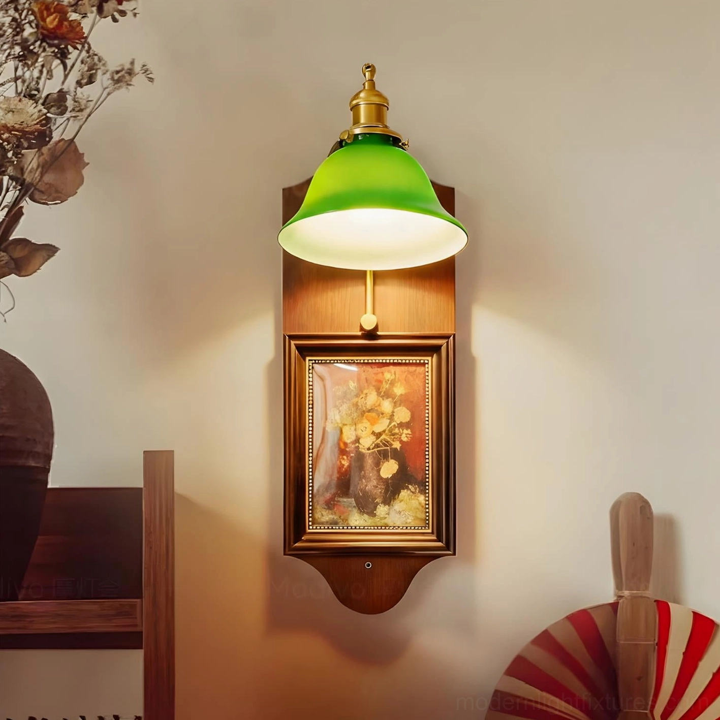 Decorative wall sconce with glowing emerald glass shade and brass finial against vintage dried flower decor