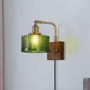 Green glass pressed pattern wall sconce with curved brass arm and wood mounting plate - three-quarter angle