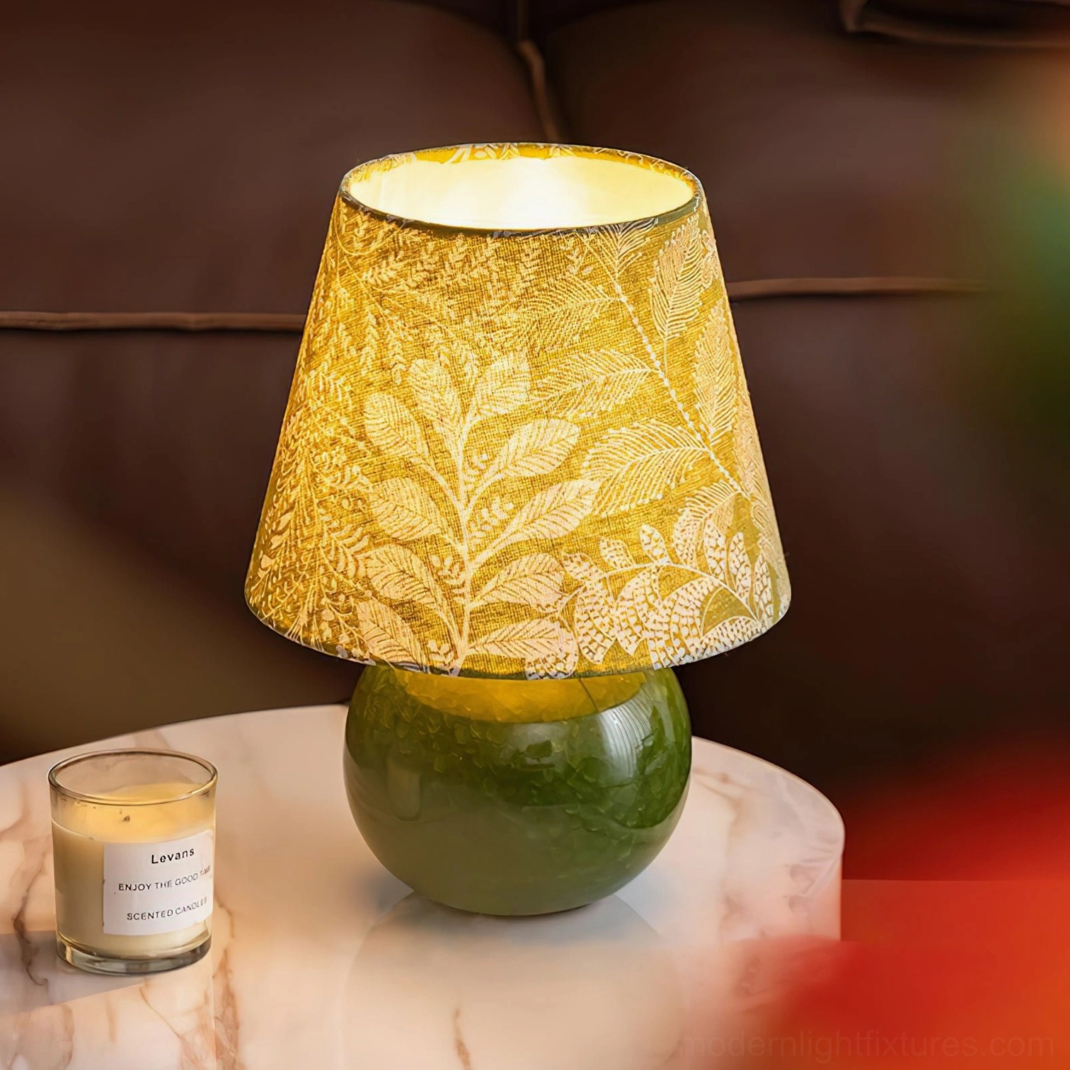 Green table lamp with leaf shade illuminated on marble surface near sofa
