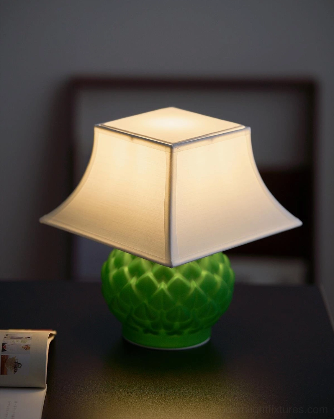 Green Petaluxe table lamp on bedroom nightstand with dark wooden headboard, cozy bedside lighting ambiance