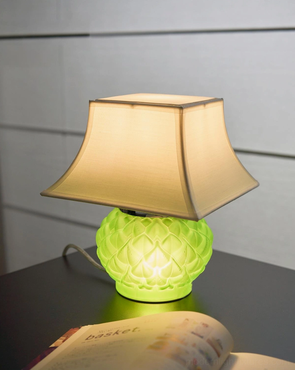 Illuminated green Petaluxe table lamp glowing on desk beside open magazine demonstrating warm ambient lighting