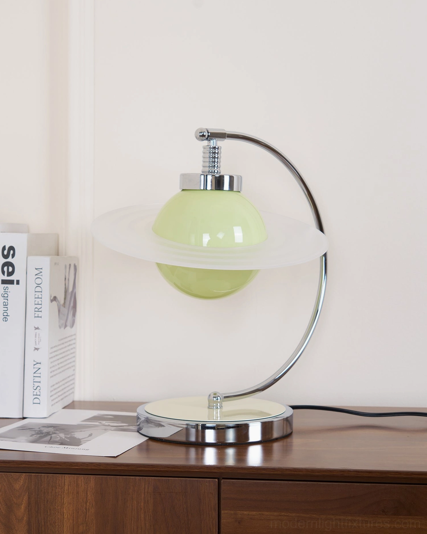 Right three-quarter view of modern green table lamp with chrome base beside decorative books on cabinet