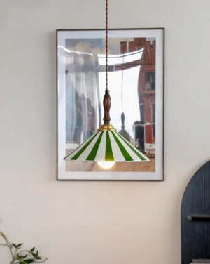 Green and white striped hand-painted ceramic pendant lamp with warm glowing exposed bulb in cozy home interior setting with wall art