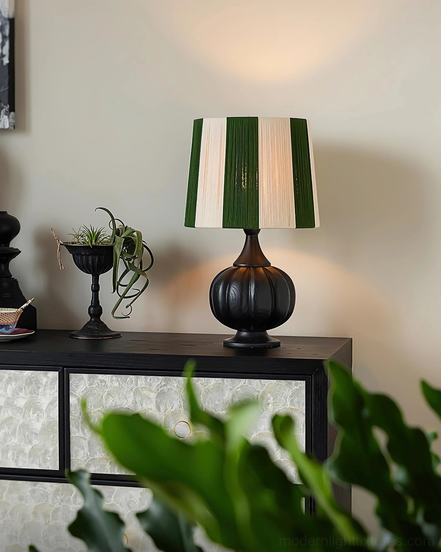 Green and cream striped wooden table lamp with black pumpkin base displayed on vintage side cabinet