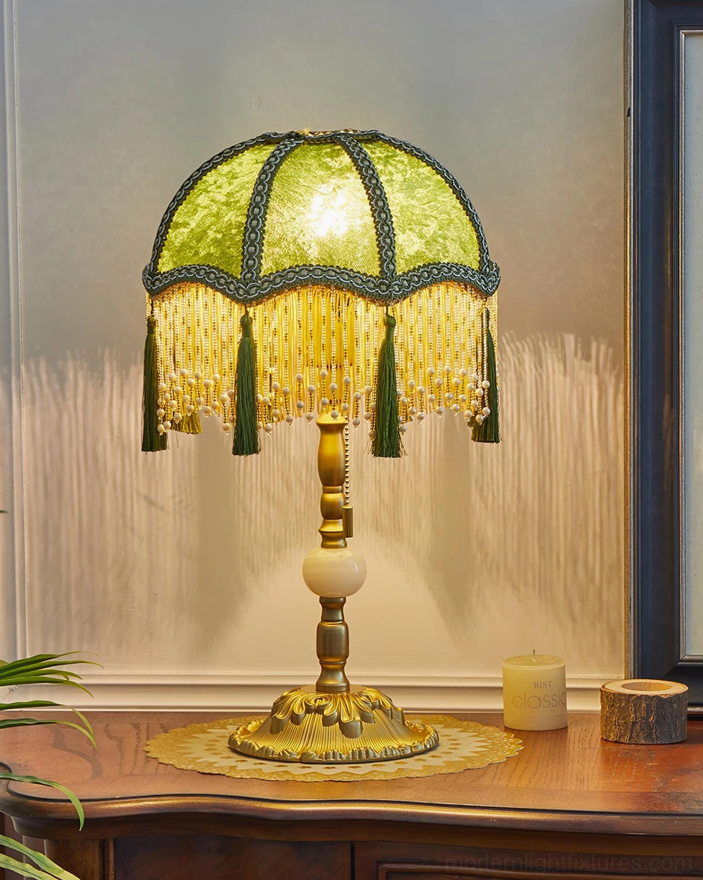 Emerald green velvet table lamp close-up showing beaded tassels and fabric texture near mirror backdrop