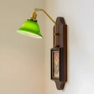 Emerald green wall sconce mounted on indoor accent wall corner, showing lit brass hardware and warm glow