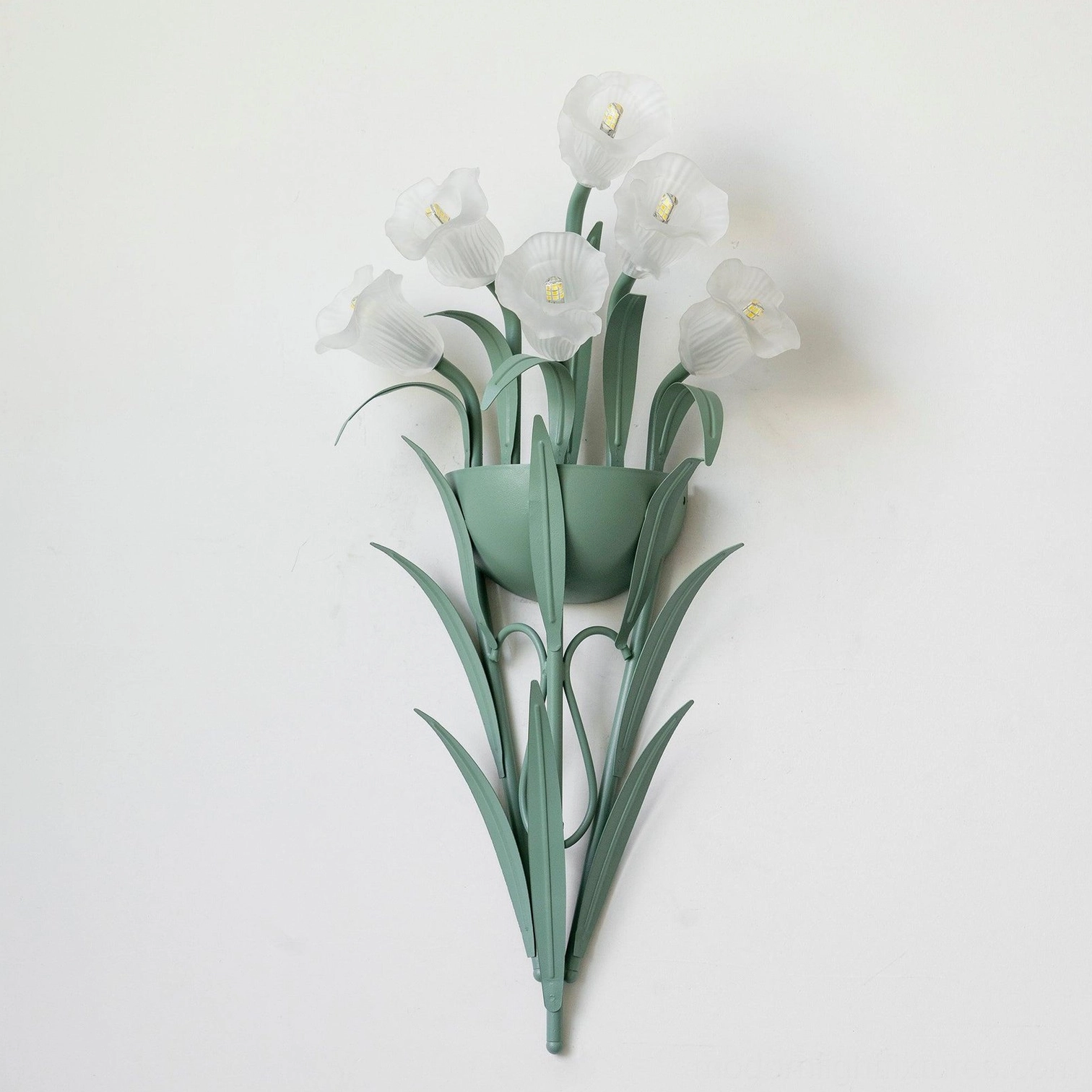 Green wall sconce with unlit white artificial flowers on white background, minimalist botanical light fixture