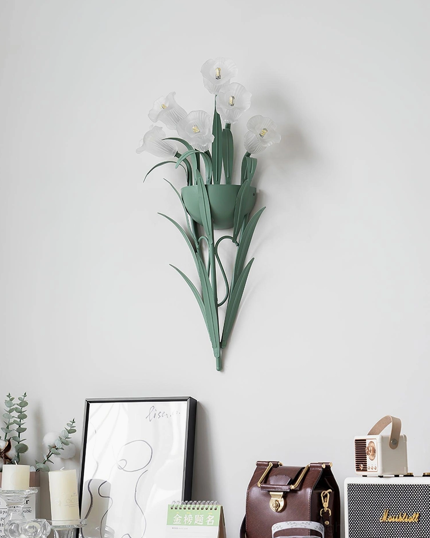 Green and white botanical wall sconce displayed on light gray wall with desk accessories, unlit modern sconce