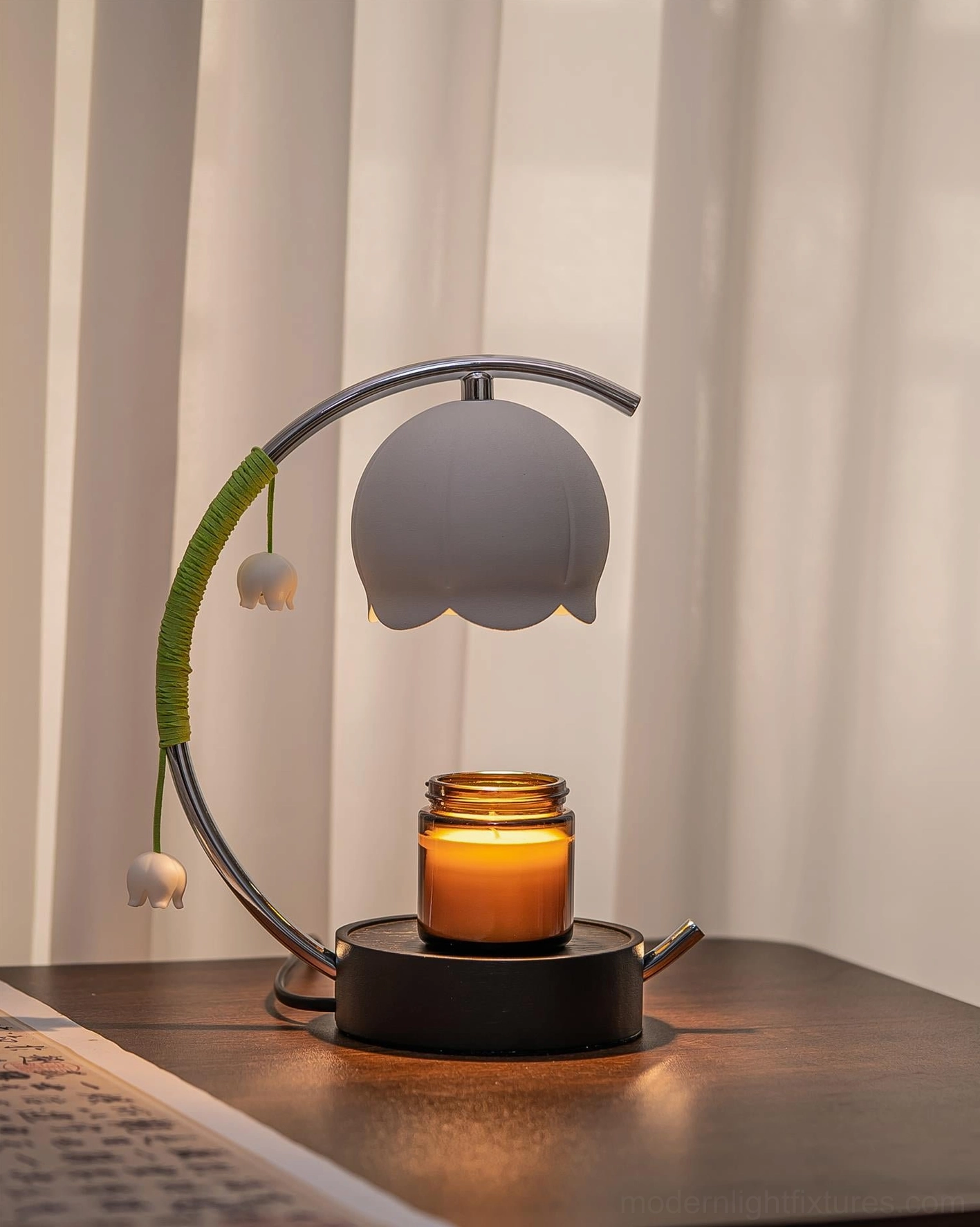 Contemporary candle warmer lamp with grey bell shade and lit scented candle jar on desk with sheer curtain backdrop