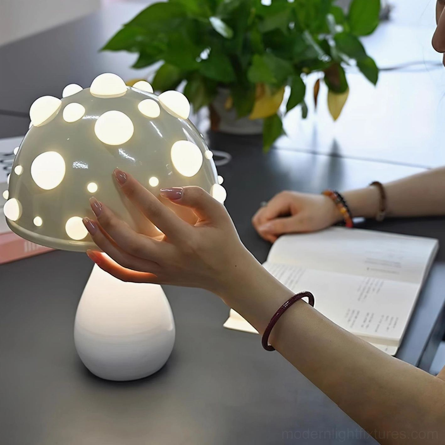 Light grey spotted mushroom table lamp close-up side view with hand interaction on home study desk, glowing LED cap