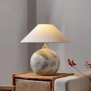 Grey and white ceramic table lamp displayed on rattan side table in living room with red floral decor and minimalist interior styling
