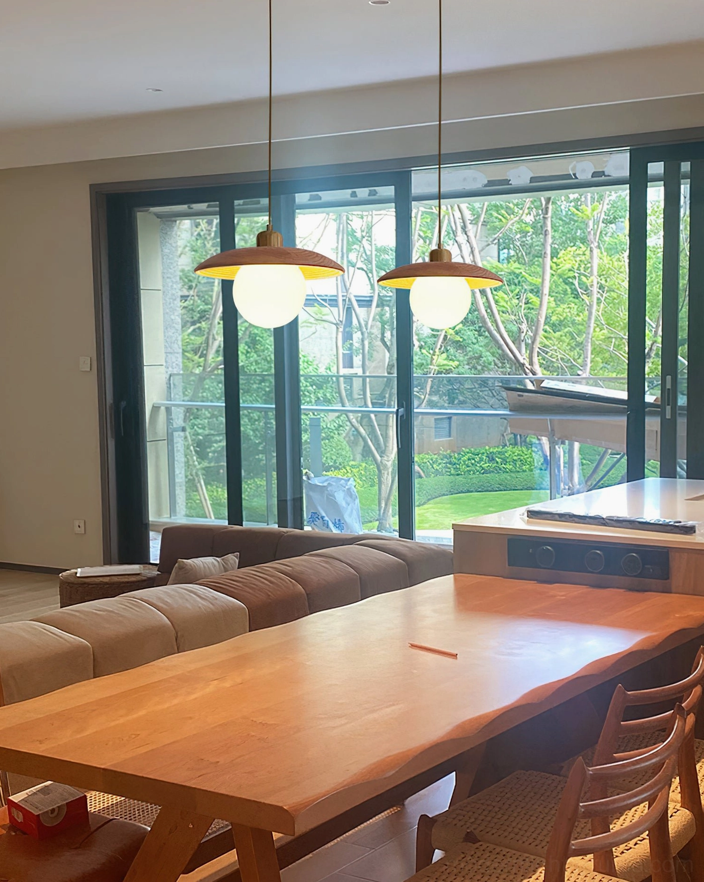 Pair of oak wood pendant lights hung over long wooden dining table in open-concept modern home