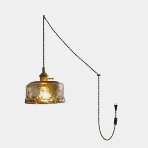 Hand-blown amber glass plug-in pendant light with brass socket holder and twisted cloth cord, studio front view
