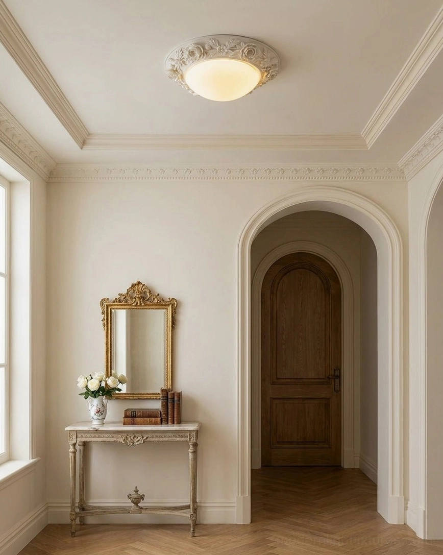 Hand-carved floral flush mount light installed in French country style entryway with gilded vanity mirror and herringbone flooring