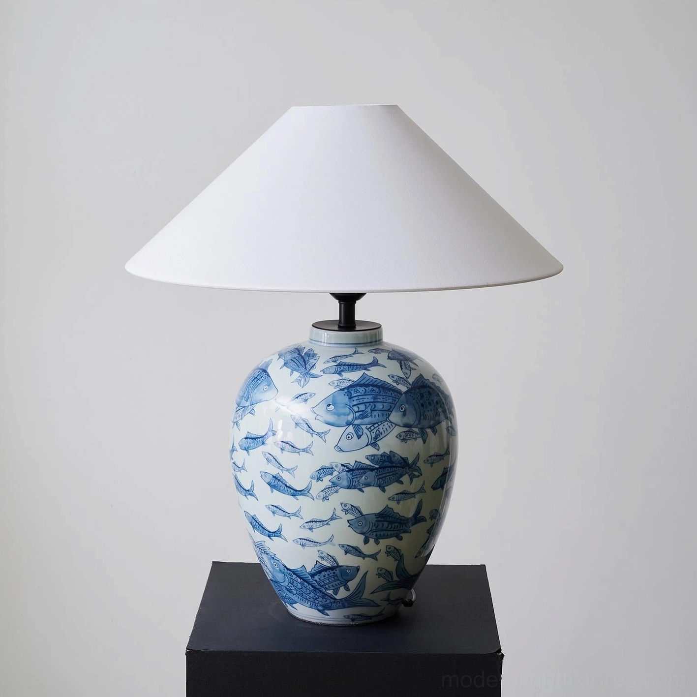 Decorative blue and white ceramic table lamp with hand-painted details, left-front studio view on black display stand