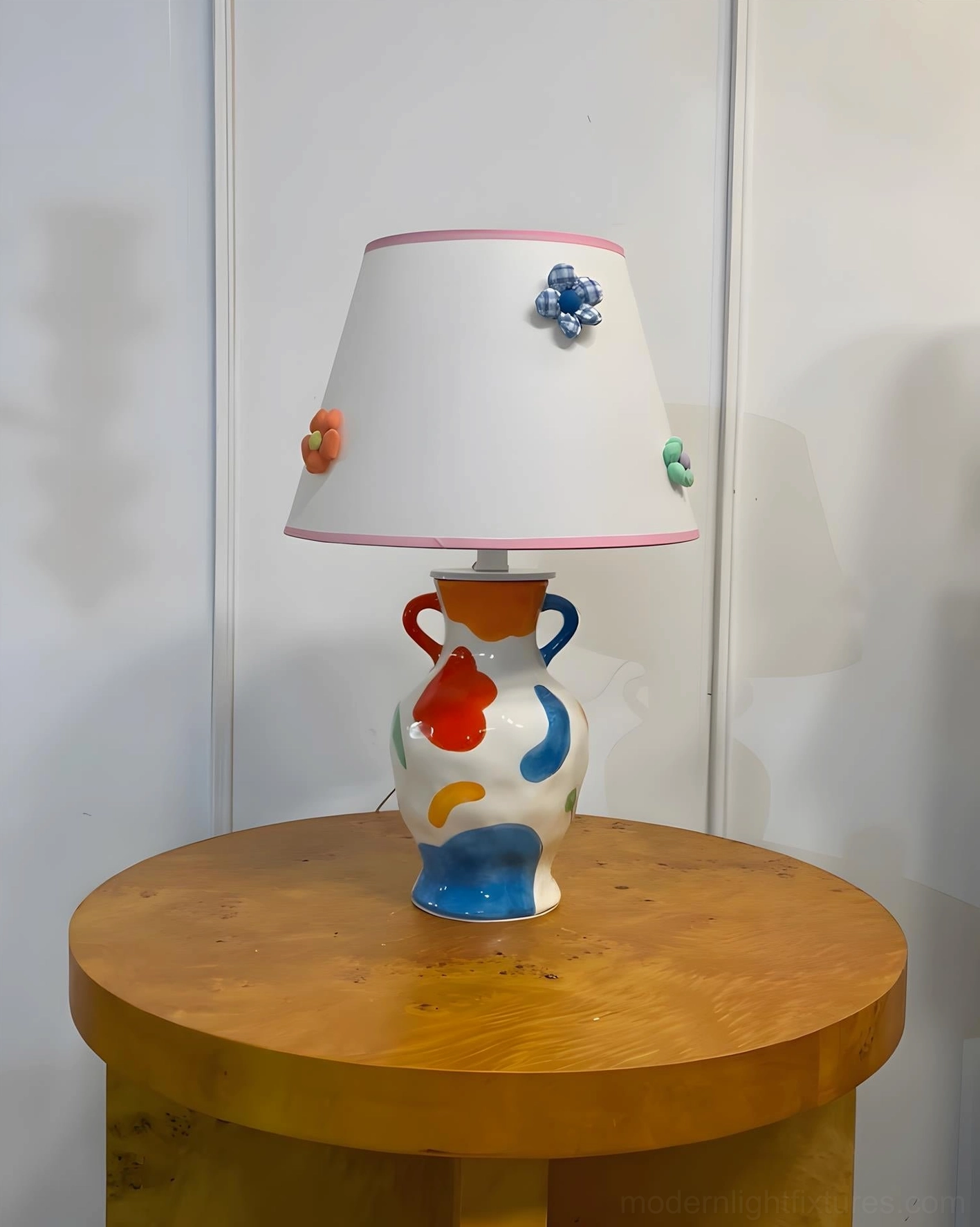Hand-painted ceramic table lamp three-quarter side view on round wooden side table, minimalist neutral backdrop showcasing full lamp shape and floral decorations