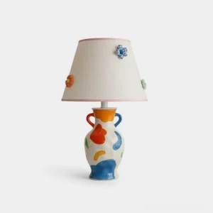 Hand-painted ceramic table lamp with multicolor abstract base and white fabric shade trimmed in soft pink with 3D floral accents, frontal studio view