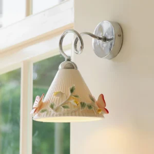 Ceramic butterfly wall sconce illuminated in home interior, warm ambient light highlighting 3D embossed floral and butterfly decorations on pleated shade