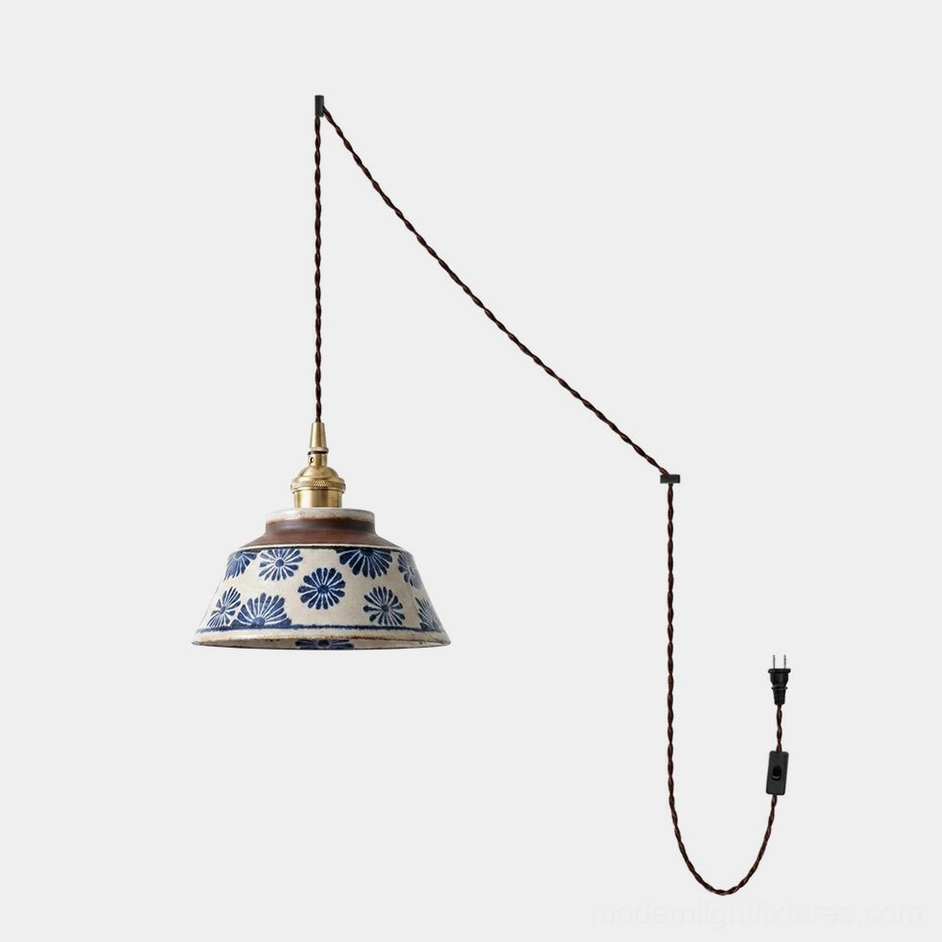 Hand-painted indigo ceramic plug-in pendant lamp with chrysanthemum pattern on warm cream stoneware, brass socket, and twisted braided cord on white background