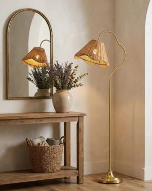 Rattan arc floor lamp in warm gold finish positioned in entryway beside arched mirror and wooden console table