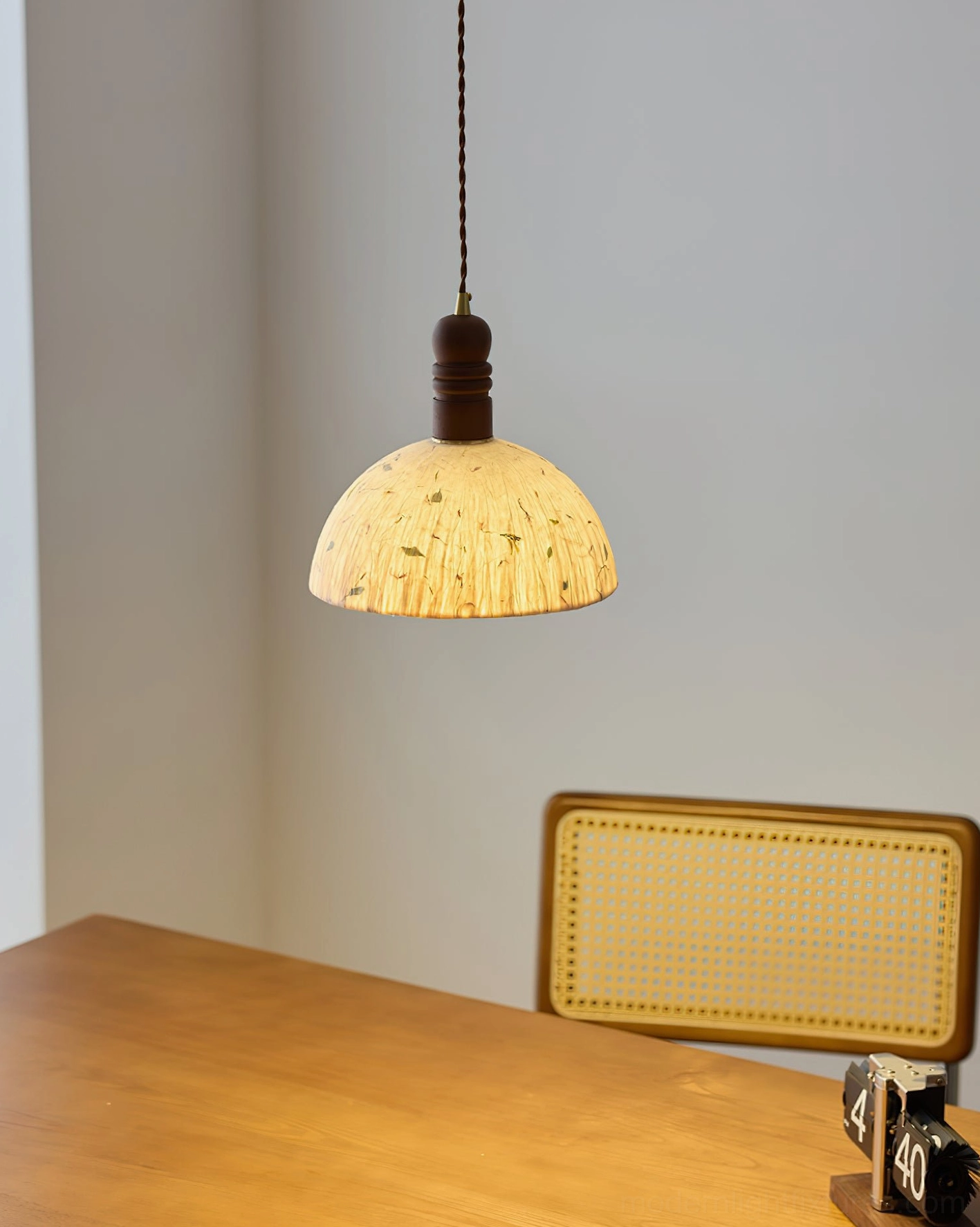 Suspended dome pendant lamp over wooden dining table with rattan chairs, wabi-sabi style interior