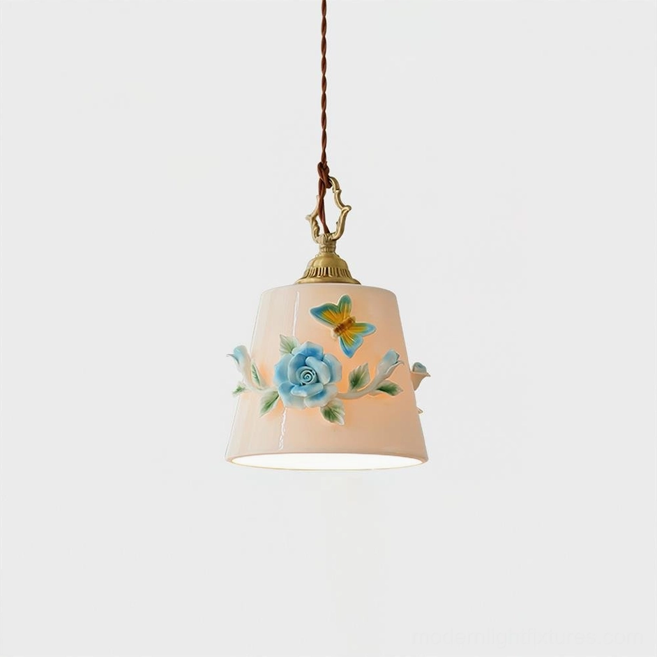 Handpainted floral ceramic pendant light with antique brass suspension, cream-white shade featuring detailed rose and butterfly botanical motifs, front studio view