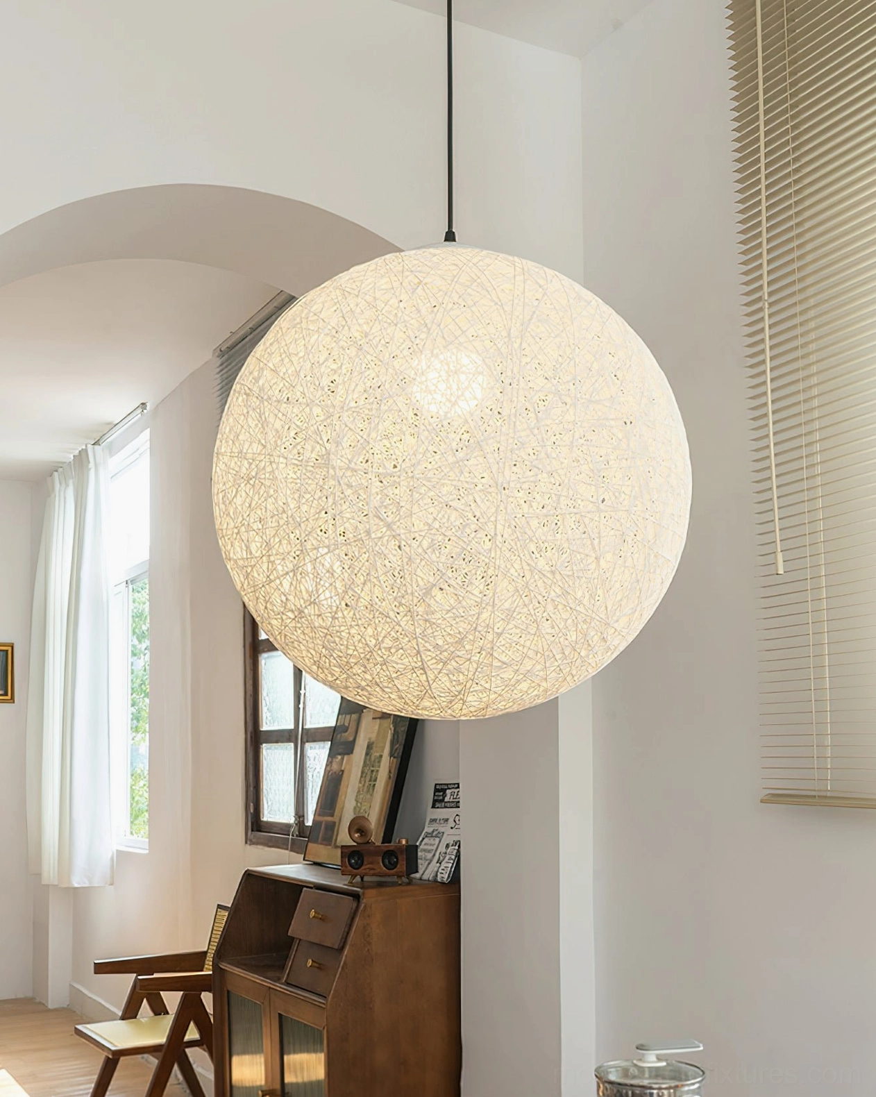 Beige hemp woven sphere pendant lamp side three-quarter view above wooden desk in home office, natural lighting