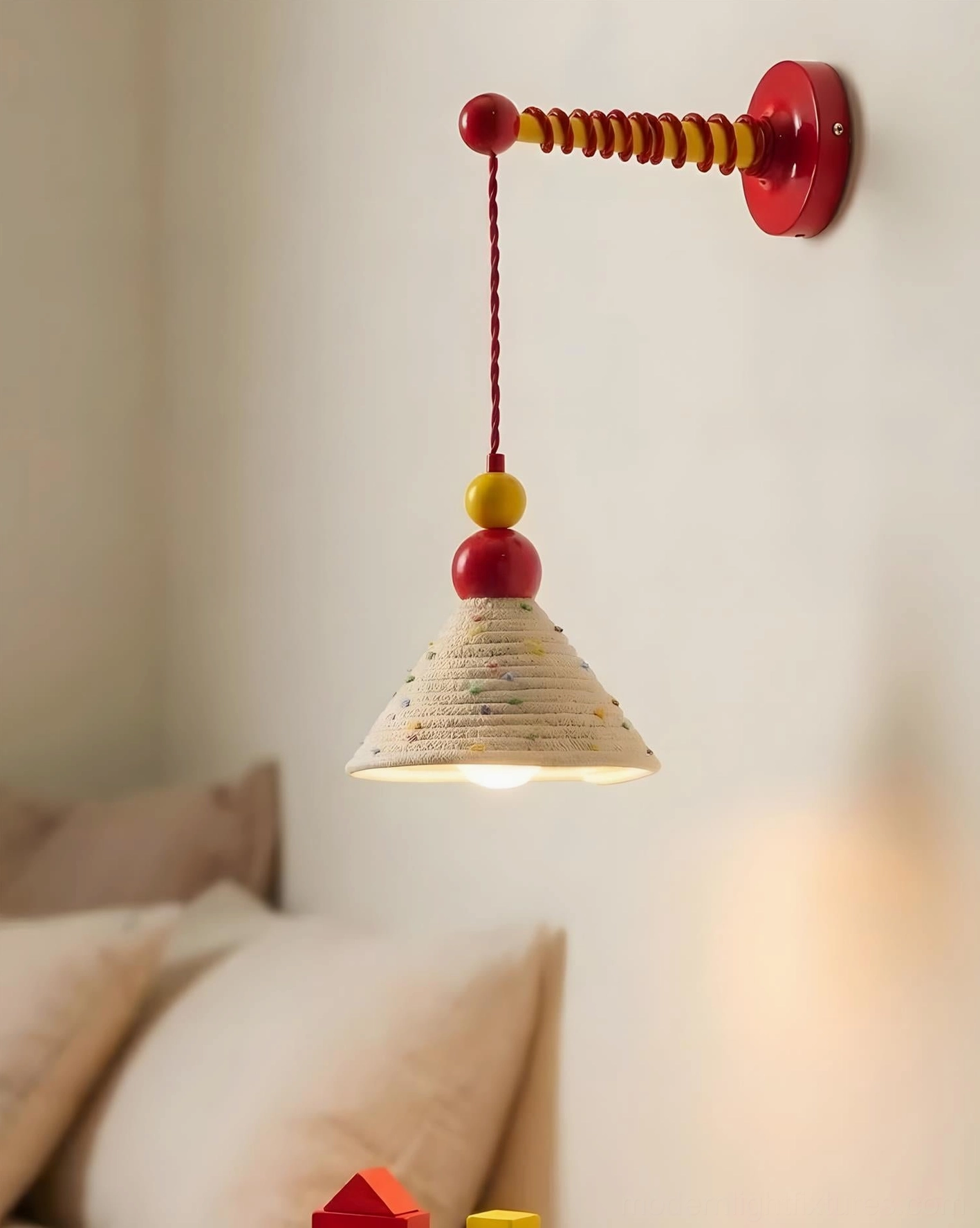 Colorful wall mounted sconce installed beside bedroom bedside table with red metal mount and sculptural bead detailing