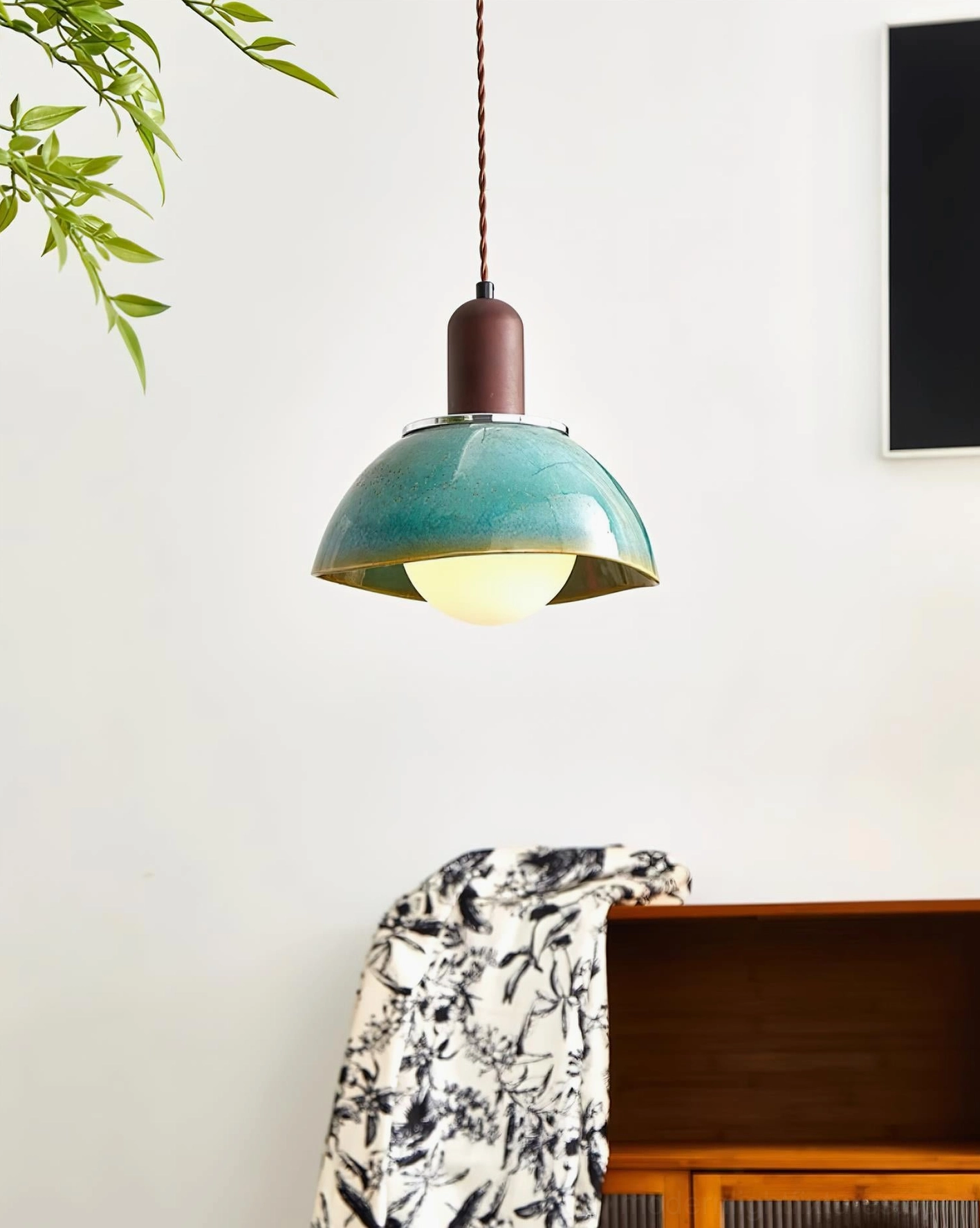 Modern ceramic pendant light hanging above wooden cabinet in Nordic-inspired home interior with patterned textiles