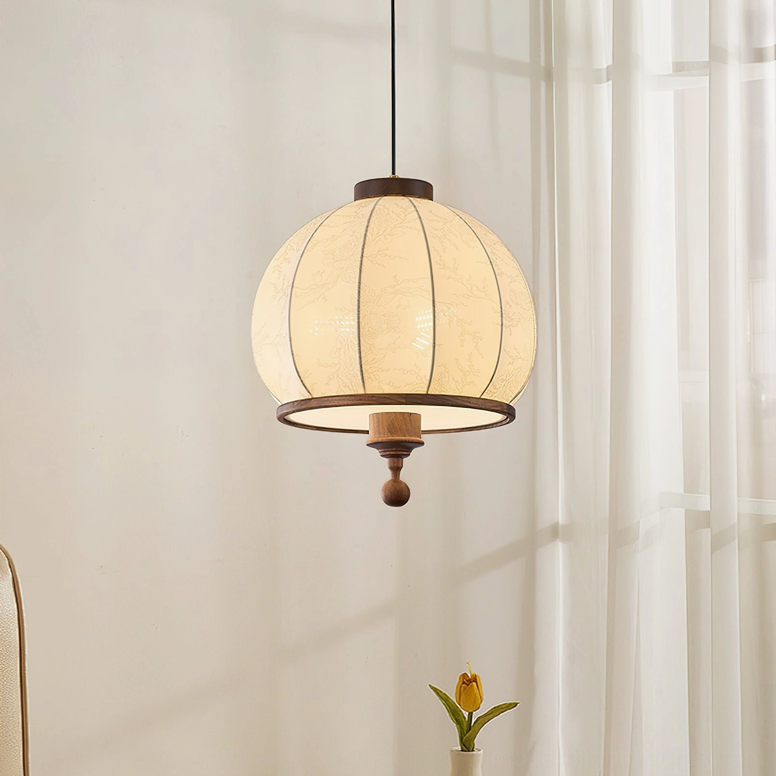 Globe-shaped fabric pendant lamp with warm beige shade and dark wood base near sheer curtains