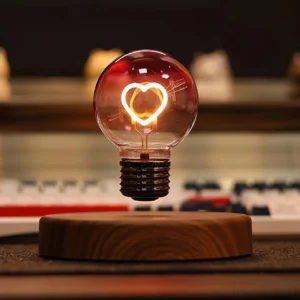 Close-up view of magnetic levitating heart lamp with pink-tinted glass globe and glowing warm LED on desk surface