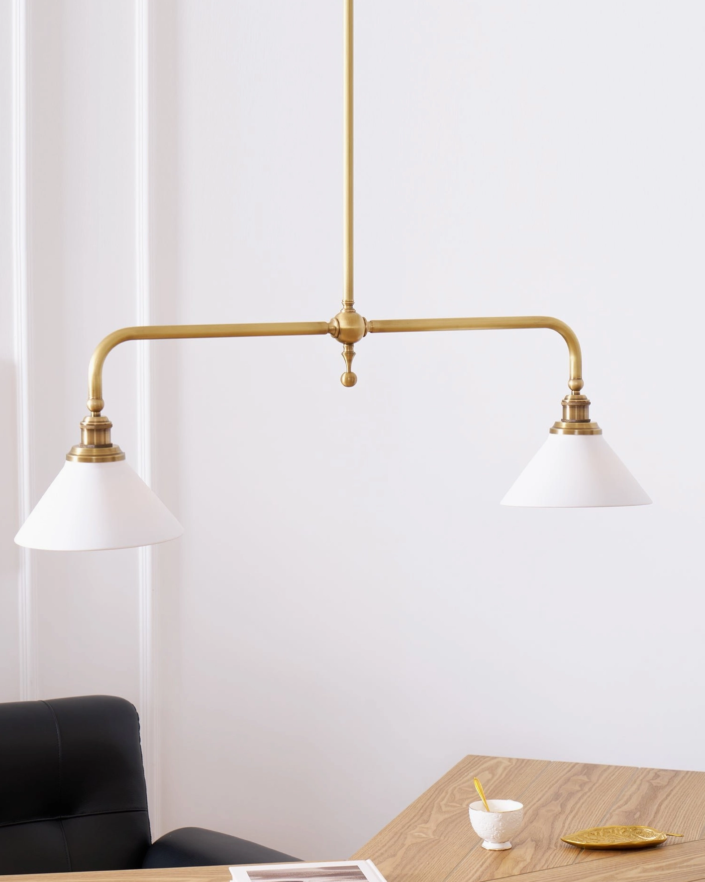 Heirloom-style linear pendant light with aged brass hardware and white ceramic shades in sophisticated interior design