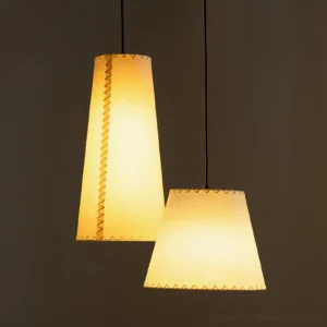 Hemline fabric pendant light illuminated close-up showing warm yellow glow through parchment shade with whip-stitch trim