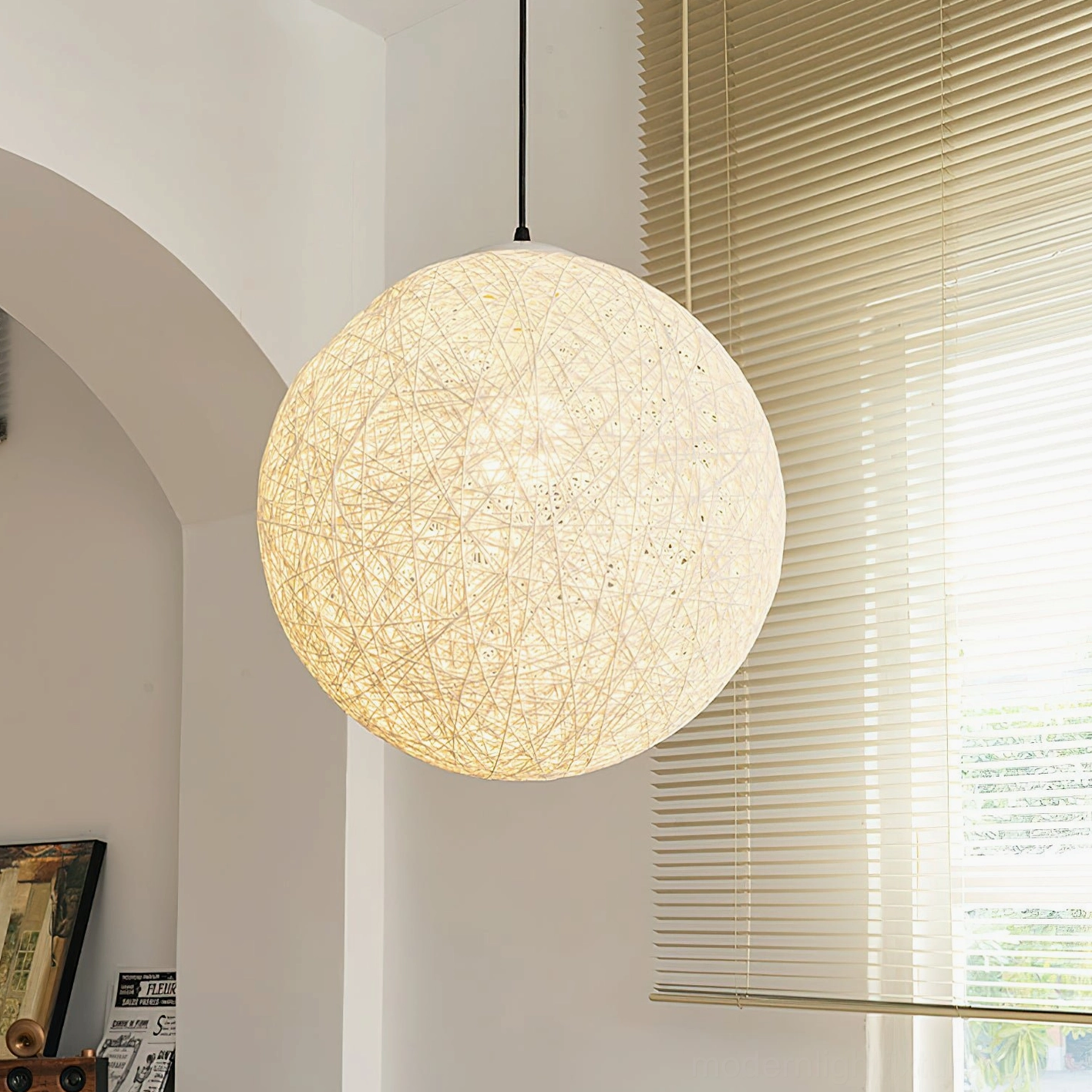 Beige hemp woven pendant lamp three-quarter angle view in residential interior with arched doorway and window blinds, warm ambient lighting