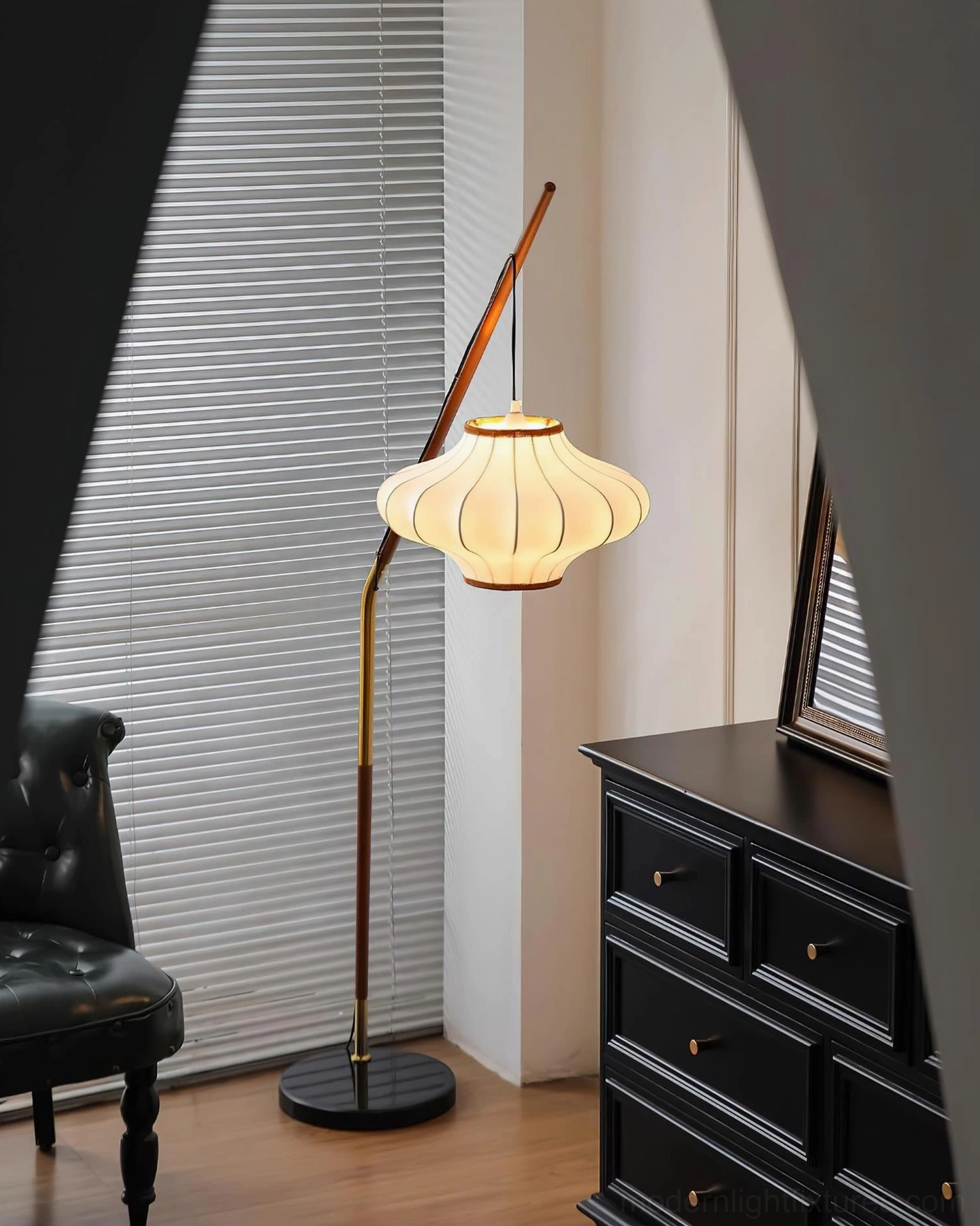 Glowing Hikari arc floor lamp with fabric shade next to black leather chair in mid-century interior
