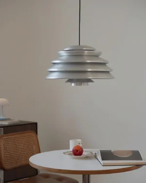Modern brushed silver Hive pendant lamp hanging above dining table in Nordic-inspired interior, overhead perspective showing layered disc construction