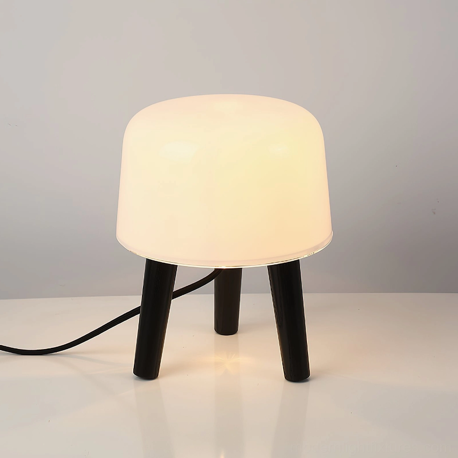 Front three-quarter view of illuminated milk glass table lamp with black wood base showing warm frosted glass diffusion
