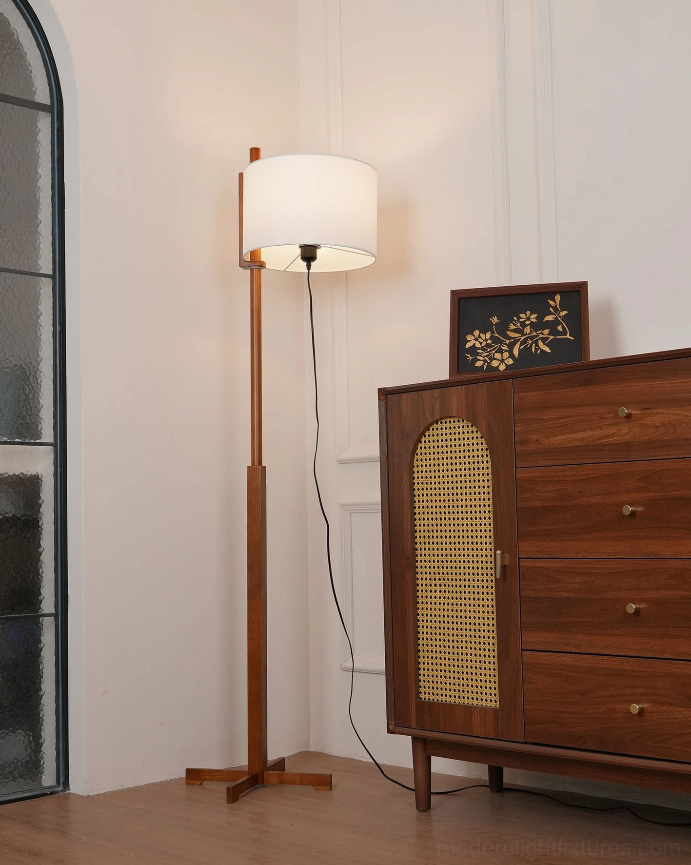 Modern walnut wood floor lamp illuminated at night, soft warm light diffusing through white cylindrical fabric shade