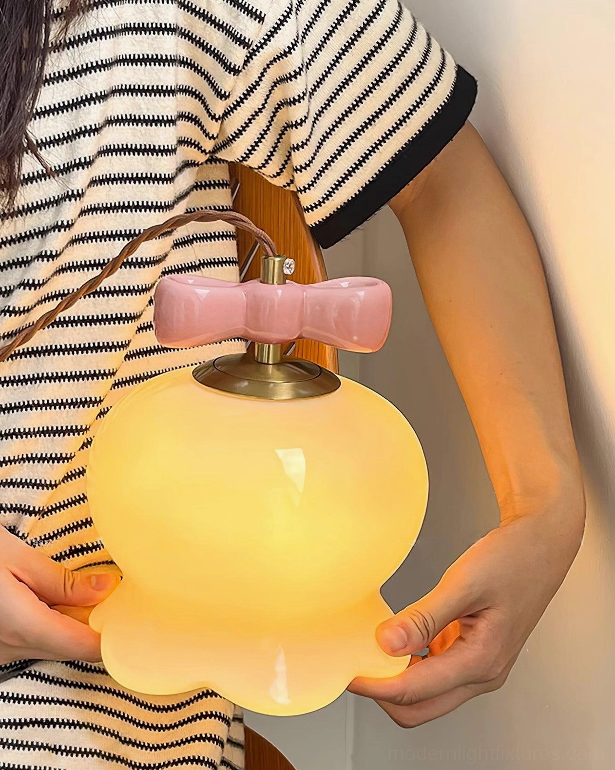 Illuminated pink ceramic pendant light with bow top detail and warm glow