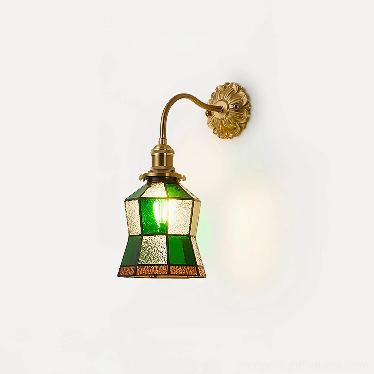 Illuminated vintage stained glass wall sconce with emerald glass shade and ornate brass base, front three-quarter view showing warm light glow