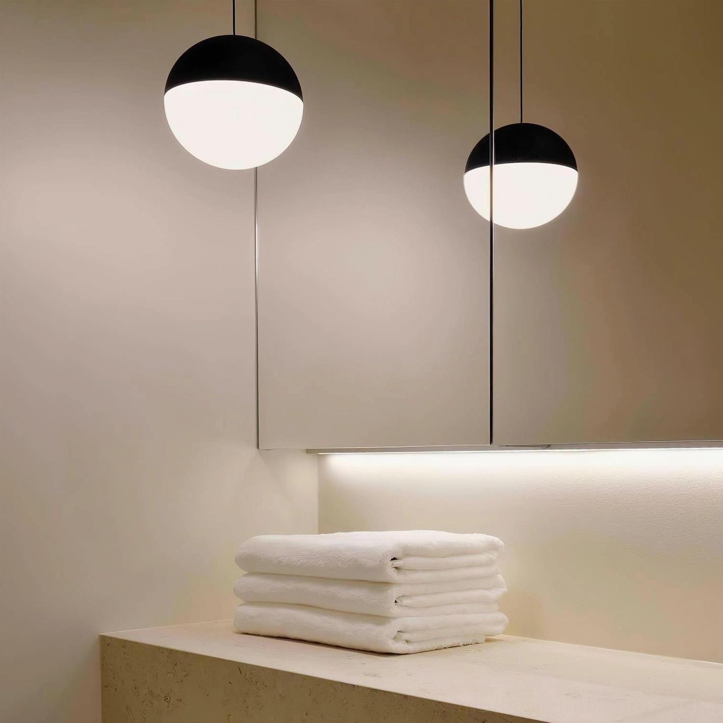 Two-tone spherical pendant light illuminated in modern bathroom vanity, warm lighting with exposed cable, contemporary fixture