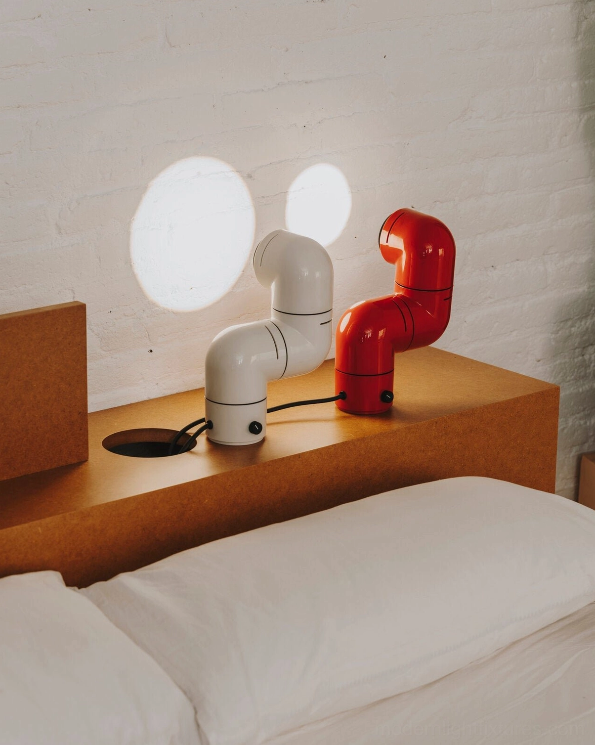 White and red tubular table lamps on bedroom nightstand both projecting light spots