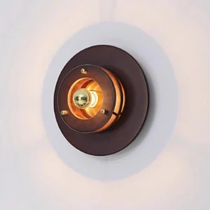 Jaima industrial wall sconce front view with cast shadow highlighting the dimensional layered construction and central metallic light core