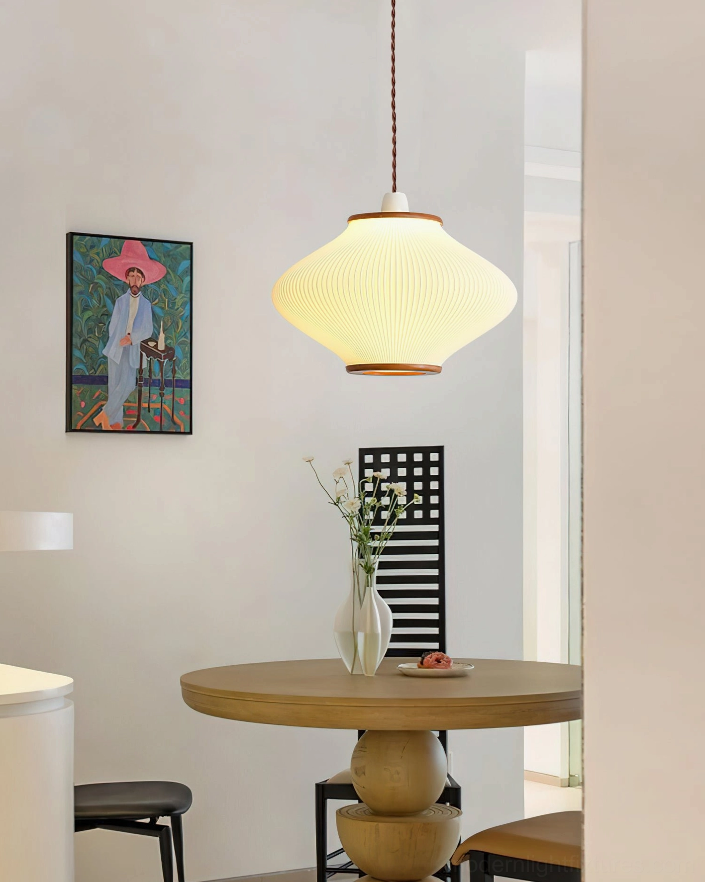 Modern pendant light with pleated acrylic shade in boho dining nook with round wooden table, side angle view