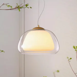 Contemporary double-layer glass pendant light side angle showing dome shape with warm interior glow and foliage backdrop