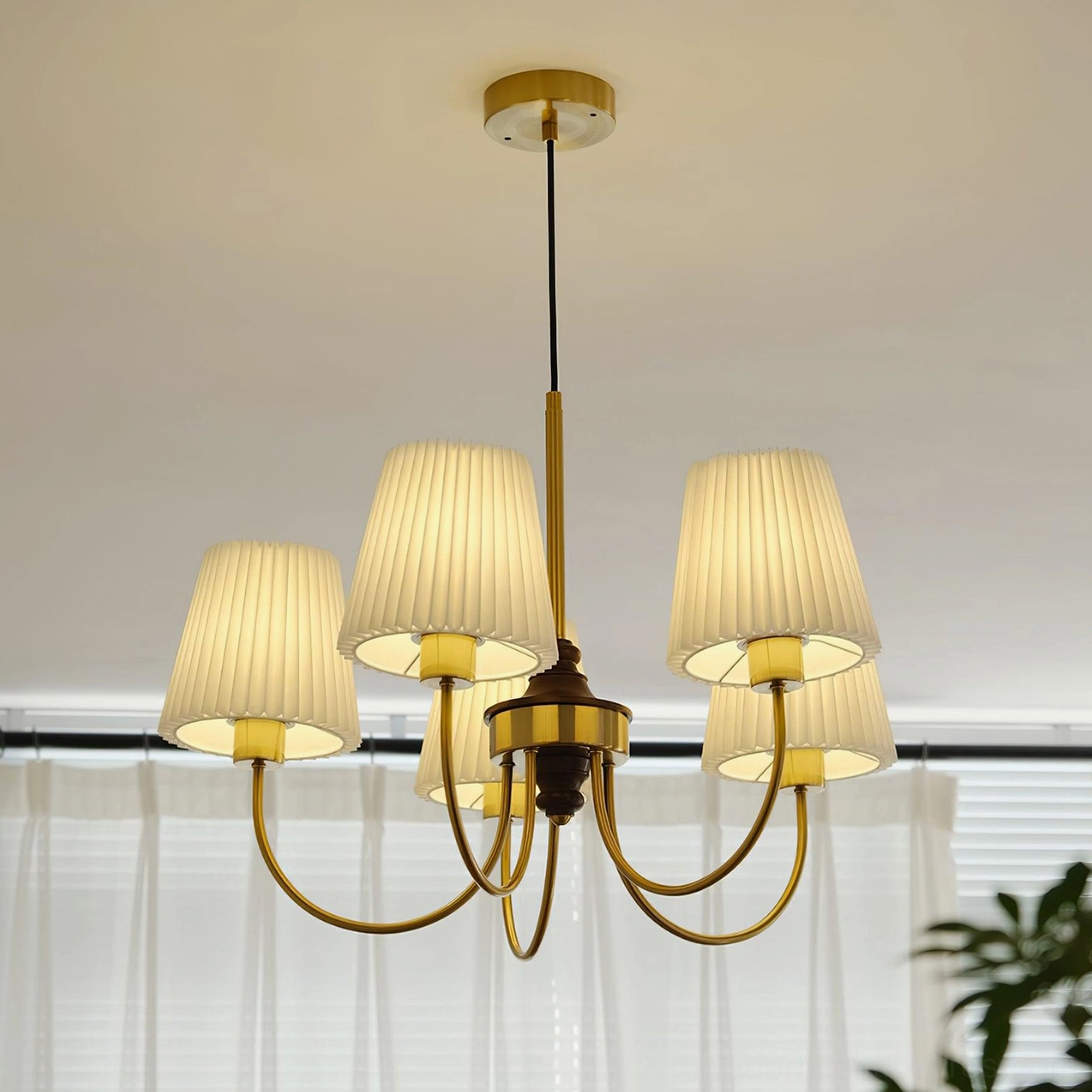5-light brass chandelier by Jeremiah with curved gold metal arms and pleated shades in modern living room with plants